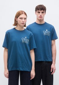 Μπλε βαμβακερά T-shirt με κοντά μανίκια, στρογγυλή λαιμόκοψη και λευκό λογότυπο Calvin Klein στο μπροστινό μέρος. Χαλαρή εφαρμογή με λεία υφή.