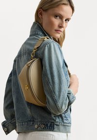 Borsa beige con un design arrotondato, in pelle liscia e con hardware dorato. Indossata a spalla, abbinata a una giacca di jeans.