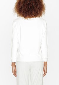 Felpa bianca con maniche lunghe, in cotone, con scollatura rotonda e polsini a coste, abbinata a pantaloni a righe grigio chiaro.