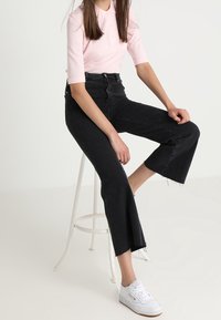 Černé džíny s vysokým pasem, zkrácenou širokou nohavicí a roztrhanými lemy, doplněné světle růžovým polo tričkem s krátkým rukávem a bílými teniskami.