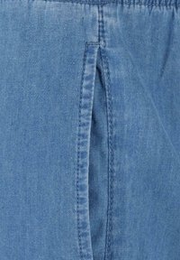 Denim stof i lys blå med en synlig syet søm. Har en sidelomme og en glat tekstur, der fremhæver afslappede designelementer.