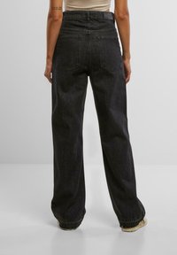 Hoch taillierte schwarze Denim-Jeans mit lockerer Passform, ausgestattet mit zwei aufgesetzten Taschen auf der Rückseite und einer leicht strukturierten Oberfläche.