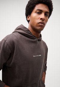 Bruine hoodie gemaakt van katoen, met een klein wit logo op de borst. Het ontwerp heeft ribgebreide manchetten en zoom.