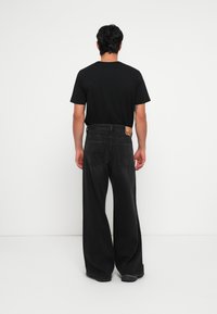 Μαύρη μπλούζα T-shirt συνδυασμένη με φαρδιά, σκούρα γκρι τζιν παντελόνια. Τα τζιν διαθέτουν πίσω τσέπες και ορατή ετικέτα μάρκας στη μέση.