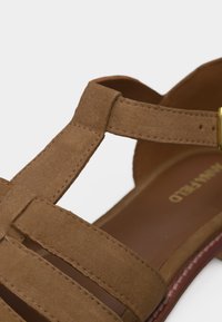 Sandale en daim marron avec plusieurs brides et une boucle dorée sur fond blanc.