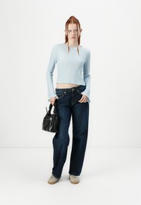 Light blue ribbed long-sleeve top with a cropped hem, paired with dark blue wide-leg jeans. Holding a black textured handbag, wearing light shoes.