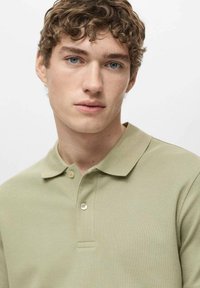 Hellgrünes Poloshirt aus strukturiertem Stoff, mit zwei Knöpfen am Kragen, kurzen Ärmeln und klassischem Design.