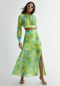 Completo in due pezzi composto da una gonna maxi plissettata e un crop top. Realizzato in un tessuto verde leggero con motivi floreali blu e uno spacco alto.