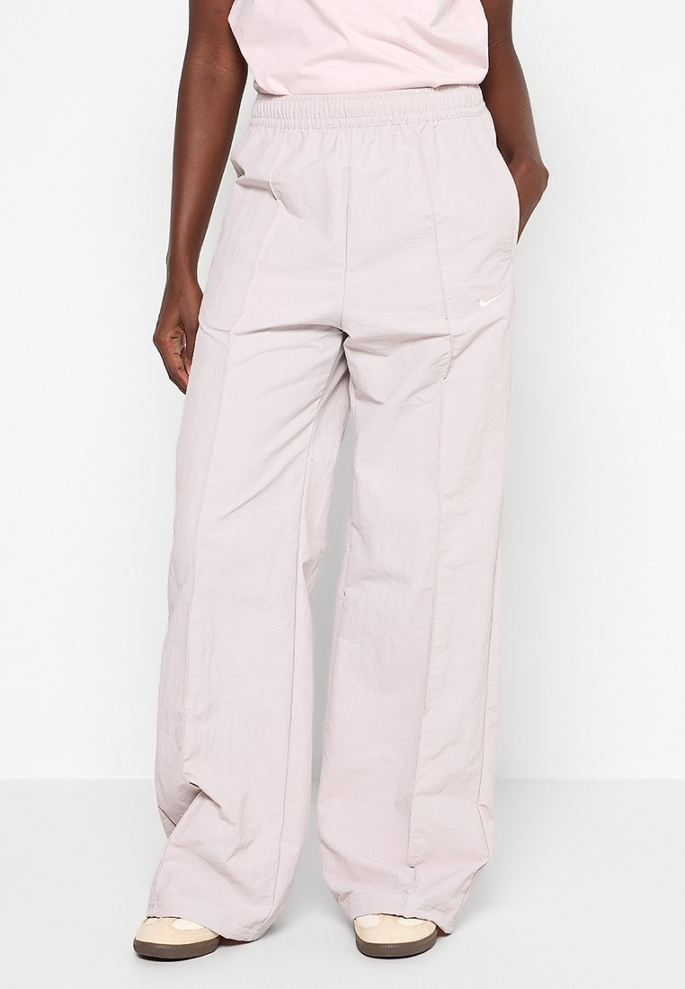 Pantalons légers de couleur rose clair, à coupe décontractée, fabriqués en tissu léger ; dotés d'une taille élastique et de poches latérales. Petit logo Nike sur le devant.