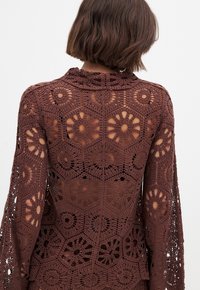 Top all'uncinetto marrone con un intricato motivo floreale, maniche lunghe e un collo alto, con spazi aperti che creano un effetto pizzo.