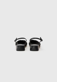 Fekete slingback cipők szőtt textil felsőrésszel, kis tömbsarokkal és állítható bokapánttal. Sima textúrájú, tartós talppal.