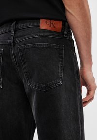 Blugi din denim închis, cu o textură ușor decolorată. Prezintă un etichetă din piele Calvin Klein pe talie și buzunare clasice la spate.