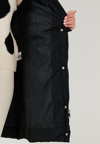 Chaqueta acolchada negra con un exterior liso y brillante, que cuenta con cierre de cremallera, botones a presión y un forro acolchado.