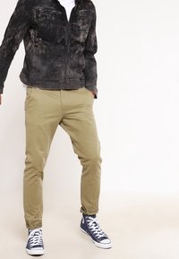 Svart, slitna jeansjacka med två bröstfickor, parat med khakifärgade slim-fit-byxor och blå högskoor.