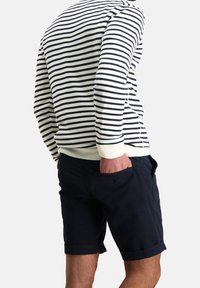 Striped white and navy sweater with ribbed cuffs, paired with navy shorts. Shorts feature a side pocket, both clothing items have a casual fit.