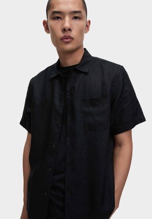 Camicia nera a maniche corte con bottoni, realizzata in tessuto leggero, con taschino sul petto e vestibilità comoda, caratterizzata da una sottile texture.