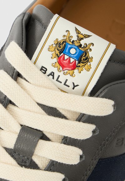 Γκρι δερμάτινο αθλητικό παπούτσι με κορδόνι στο χρώμα της κρέμας, έντονο λογότυπο με σήμα και υφασμένη πλευρική όψη σε ναυτικό μπλε χρώμα.