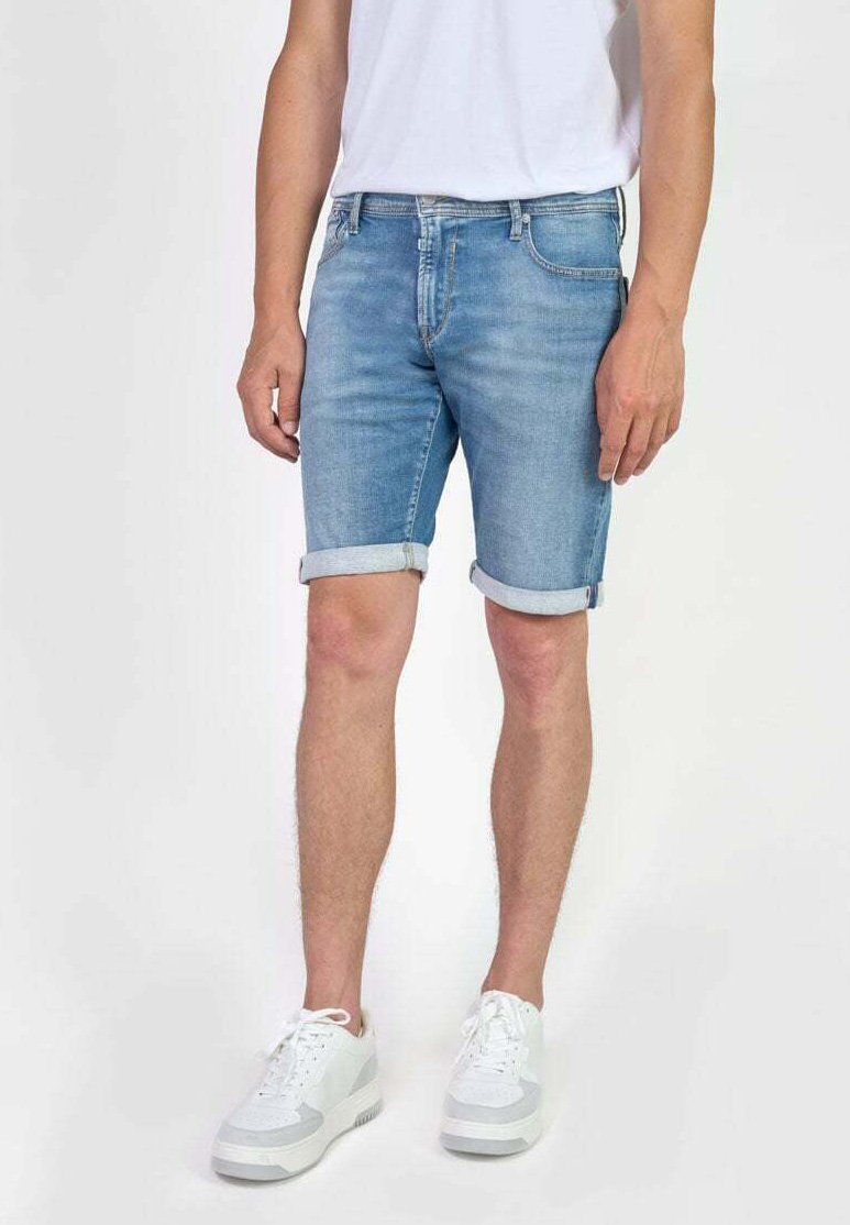 Shorts en denim bleu clair, avec des ourlets retroussés, un design à cinq poches et une taille standard. Portés avec des baskets blanches.