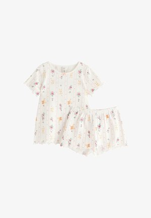 Jong meisje staat blootsvoets en draagt een wit pyjamaset met bloemen- en konijnenprints, korte mouwen en gerimpelde randen.
