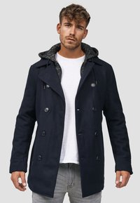 Marine peacoat med dobbeltknappede knapper og en grå mønstret hetteforing. Har en strukturert design og en midtlengde kutt.