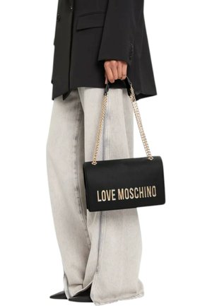 Borsa a tracolla nera in pelle con logo dorato "LOVE MOSCHINO". Presenta una cinghia a catena e una forma rettangolare. Indossata con jeans a gamba larga grigio chiaro.