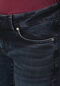 Calças de ganga escuras com um design clássico, estilo de cinco bolsos e costuras subtis. O material tem uma textura suave com ligeiro brilho.