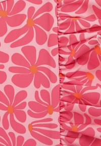Rozā ziedu audums, kurā ir lieli ziedi ar oranžām centrālajām daļām. Vienā pusē ir gubojoša apdare, kas rada tekstūru un vizuālu interesi.
