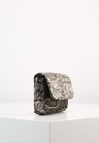 Piccola borsa rettangolare con superficie in paillettes argentate e nere, dotata di chiusura a patta e dettaglio testurizzato sul fondo.