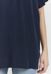 Top blu navy a maniche corte realizzato in un tessuto liscio, con una vestibilità morbida, colletto rotondo e un leggero curvatura all'orlo.