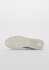 Shoe sole features a textured white rubber design with a blue and black striped upper section, highlighting grip and durability.