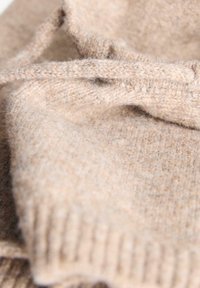 Maglione beige lavorato a maglia in morbida lana, con polsini a coste e una finitura texturizzata, con fili sciolti visibili.