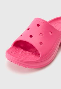 Sandale en caoutchouc rose avec bout ouvert, plusieurs trous de ventilation, semelle texturée et surface lisse. Logo de la marque visible sur le côté.