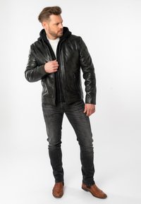 Giacca di pelle nera con zip frontale, fodera a cappuccio a coste e due tasche laterali. Abbinata a jeans in denim grigi e stivali alla caviglia marroni.