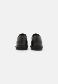 Chaussures en cuir noir avec une finition texturée, bout arrondi et semelle en caoutchouc basse. Présente un design minimaliste avec de subtils accents de couture.