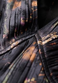 Tejido negro con pliegues y patrones florales en colores sutiles. Superficie texturizada con detalles intrincados y acabado suave.