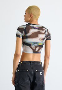 Cropped, short-sleeve top featuring a multicolored abstract pattern on a sheer fabric; worn with high-waisted black denim pants.