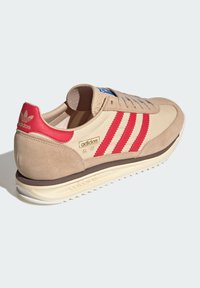 Bežiniai sportbačiai su raudonais zomšiniais dryžiais. Dangoje yra tekstūruotas viršus, paminkštinta liežuvėlė ir balta pado dalis. Šone yra "adidas SL 72" etiketė.