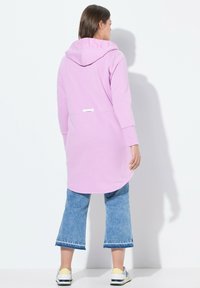 Un long hoodie rose avec un cordon de serrage à la capuche, doté d'une taille et de poignets cintrés. Associé à un jean bleu cropped et des baskets multicolores.