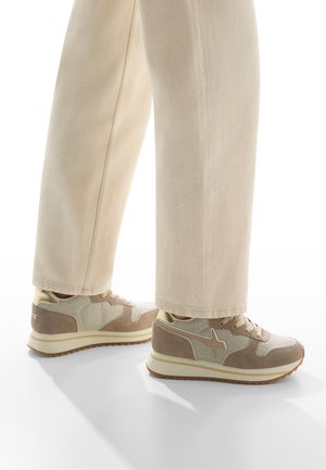 Sneakers beige in materiali mesh e suede, con suola bianca e dettagli marroni, abbinati a pantaloni larghi di colore chiaro.