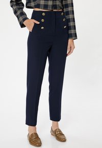 Marineblaue maßgeschneiderte Hose mit goldenen Knöpfen, hoch tailliertes Design, gerade Beine und Seitentaschen. Glatte Textur, klare Verarbeitung.