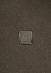 Donkerbruin stof met een gestructureerde weving. Bevat een vierkante logo-patch met "GABBIANO" in lichte kleur, omrand door een gestikte rand.