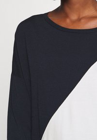 Top blu navy e bianco con una vestibilità rilassata, caratterizzato da un collo rotondo e un design a spacco diagonale. Realizzato in tessuto morbido e texturizzato.