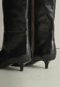 Fekete bőr, térdig érő csizmák sima felülettel, oldalsó cipzárral és keskeny, kúpos sarokkal.