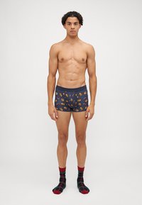 Marina boxershorts med färgglada serietidningsmotiv, med en mjuk midjeresår. Modellen bär svarta och röda rutiga strumpor.