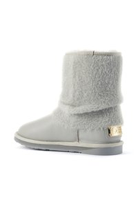 Botte en cuir gris avec un haut en fourrure grise, présentant un style replié et une plaque logo en métal doré sur le côté. Semelle plate et finition texturée.