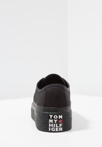Schwarze Canvas-Sneaker mit einer dicken, strukturierten Sohle. Mit einem in Weiß auf der Ferse gedruckten Logo und einem dezenten roten Sternakzent.