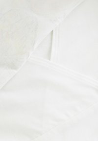 Witte laag van lichtgewicht stof met een subtiele textuurprint, die overlapt met een zachte, gladde katoenen basislaag.
