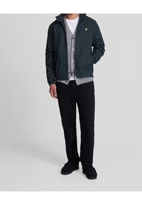 Men's dark green jacket, gray cardigan, white t-shirt, black pants. The jacket features a zip closure, elastic cuffs, and a logo. Soft textures.