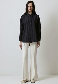 Navy striped button-up shirt with a collar, paired with cream flared pants, featuring textured fabric and a smooth finish.