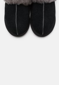 Chaussons noirs à bout fermé avec une doublure en fourrure grise autour de la cheville et une couture verticale au centre du dessus de chaque chausson.